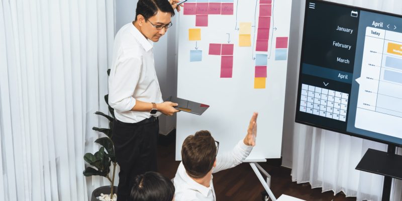 Project manager communicate and collaborate with team using project management software display on monitor, tracking progress of project task and making schedule plan at meeting table. Prudent